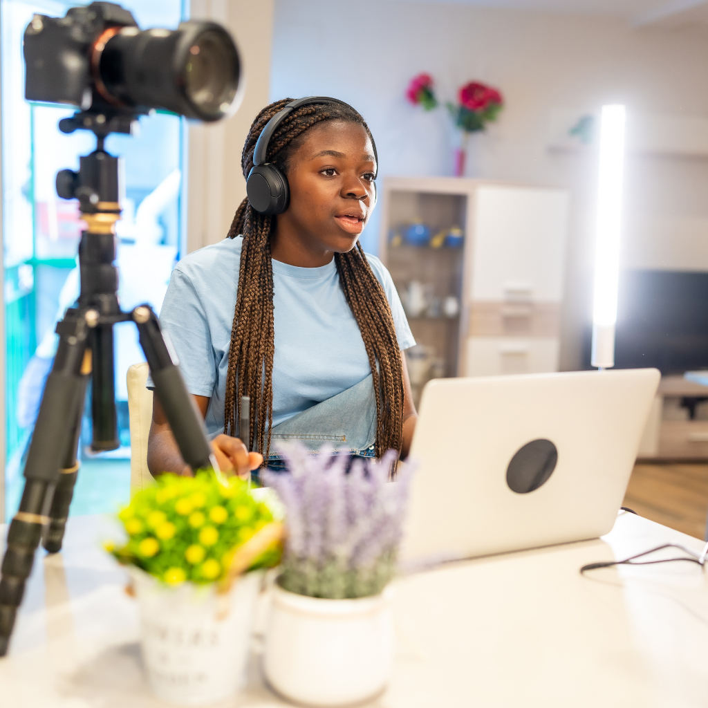 Black female content creator wearing headphones speaking into laptop with camera setup in front