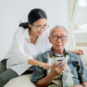Adult daughter and elderly father reviewing information together on a smartphone in a calm, supportive setting.
