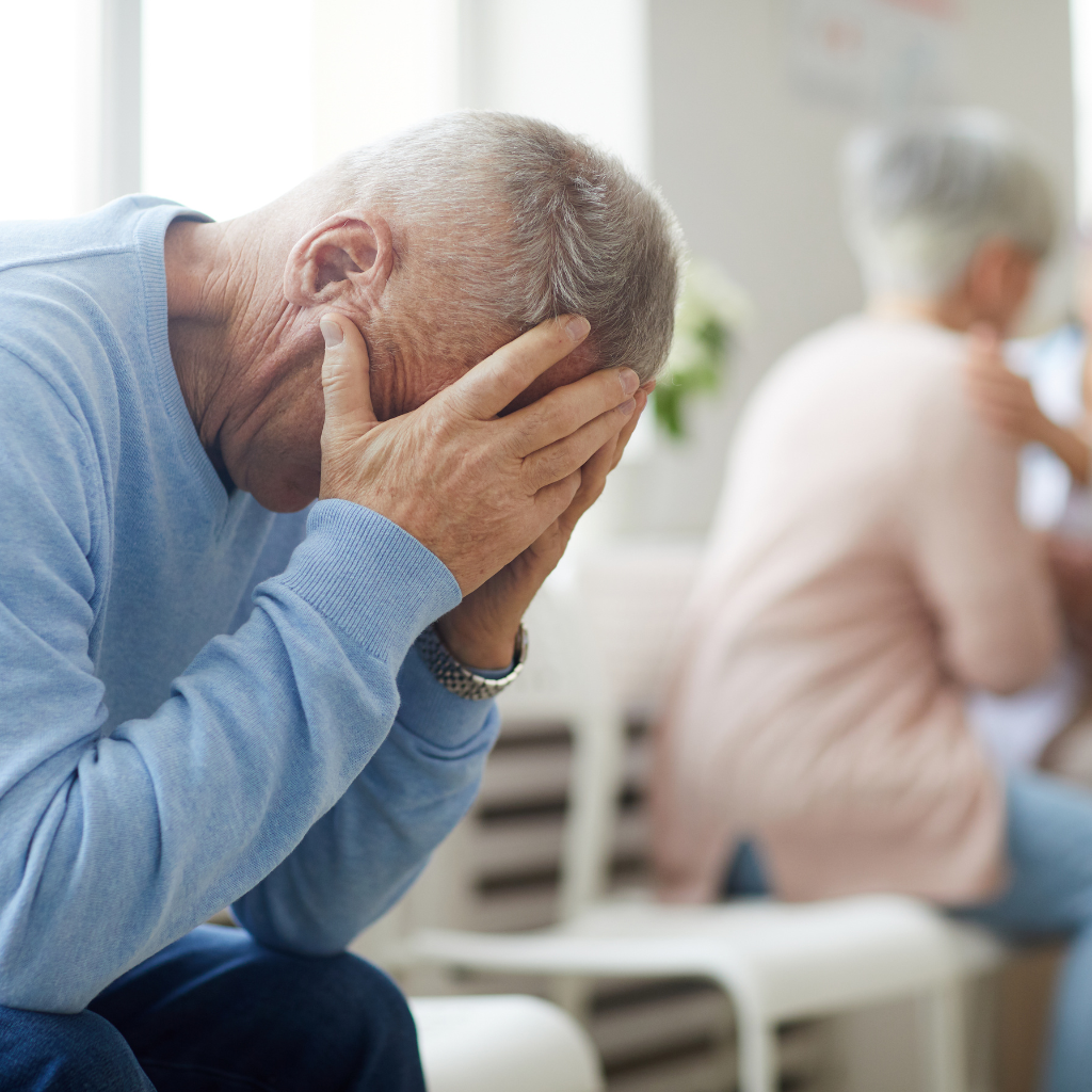 Grieving elderly man with head in hands, sitting in a waiting room after a difficult conversation or loss.