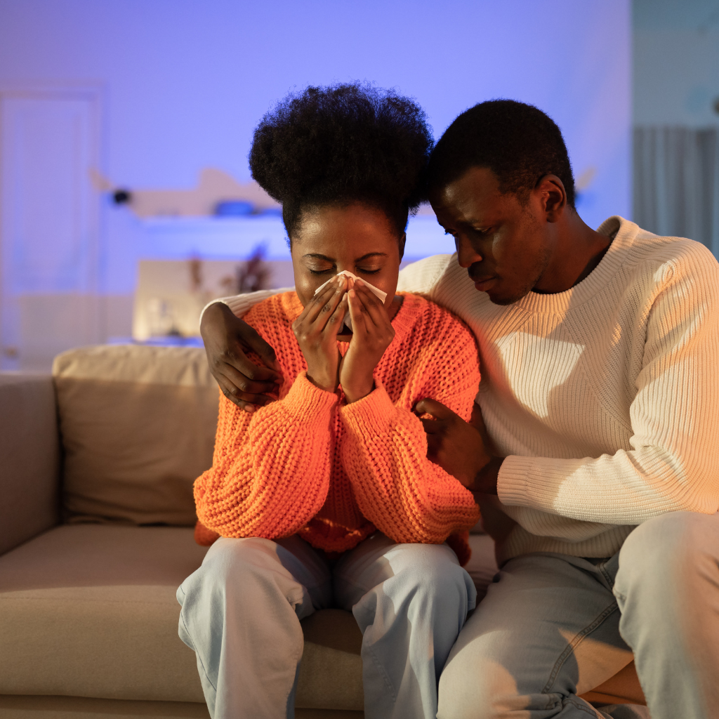 Grieving Black couple embracing each other in mourning after a loved one’s passing.