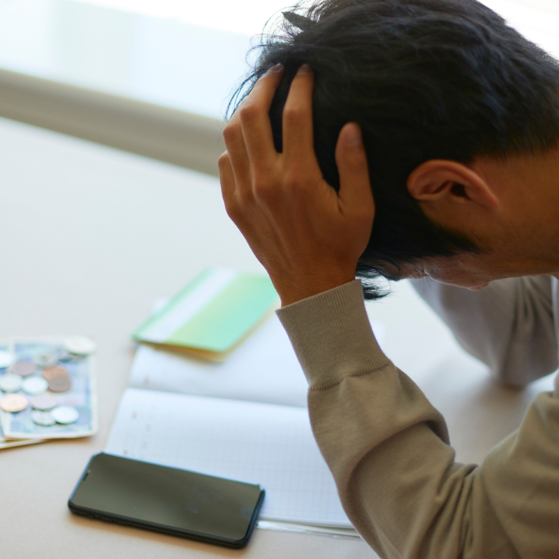 Man holding head in frustration over bills and coins, symbolizing financial stress
